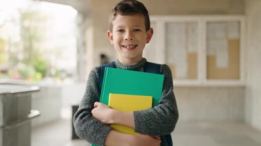 Blond child student holding books standing at school