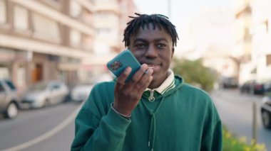 Afro-Amerikalı adam gülümsüyor. Kendine güveniyor. Akıllı telefondan konuşuyor.