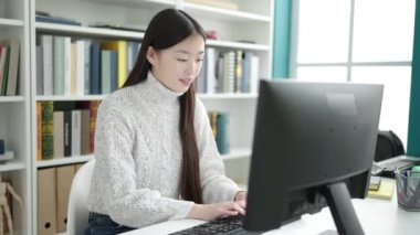 Young chinese woman student using computer stressed at library university