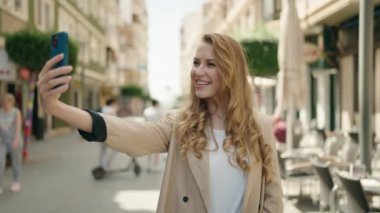 Young blonde woman smiling confident making selfie by the smartphone at street