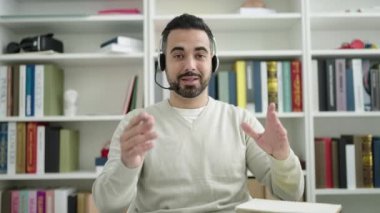 Young hispanic man student having video call writing on notebook at library university