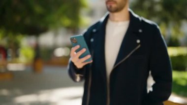 Young hispanic man using smartphone at park