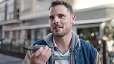 Young caucasian man sending voice message with smartphone at street