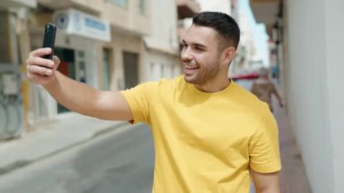 Genç İspanyol adam gülümsüyor. Sokakta akıllı telefonun yanında özçekim yapıyor.