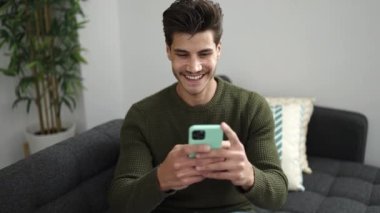 Evdeki kanepede uzanmış akıllı telefon kullanan genç bir İspanyol.