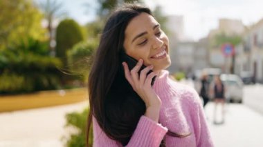 Genç İspanyol kadın gülümsüyor. Parktaki akıllı telefondan konuşuyor.