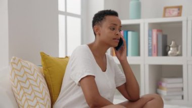 Afrika kökenli Amerikalı bir kadın akıllı telefondan konuşuyor. Yatak odasında oturuyor.
