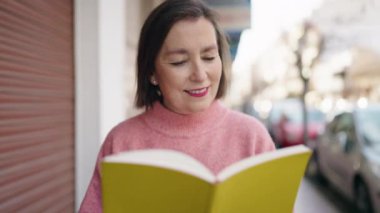 Middle age woman smiling confident reading book at street