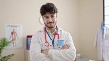 Genç İspanyol doktor gülümsüyor. Kollarını kavuşturup klinikte duruyor.