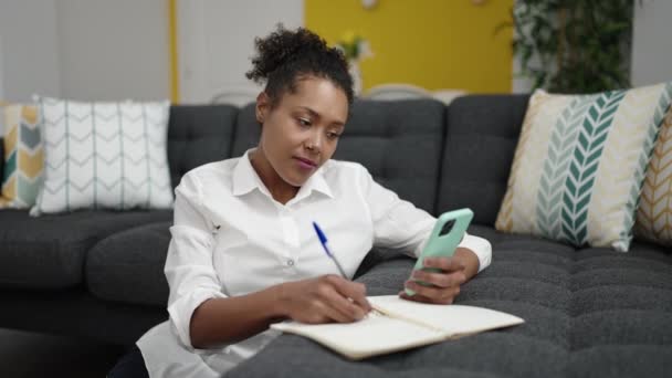 Afro Amerikalı Kadın Evdeki Defterde Akıllı Telefon Yazıları Kullanıyor — Stok video