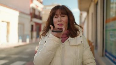 Middle age redhead woman smiling confident sending audio message at street