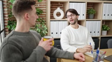 Not defterine yazan iki iş ortağı ofiste kahve içiyor.