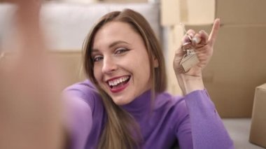 Young blonde woman having video call holding key at new home