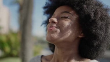 Afro-Amerikalı kadın gülümsüyor. Parkta kolları açık nefes alıyor.