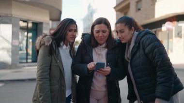 Mother and daughters smiling confident using smartphone at street