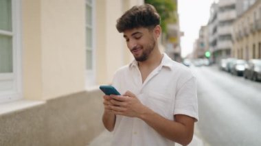 Genç Arap adam gülümsüyor. Sokakta akıllı telefondan video izlerken kendinden emin.