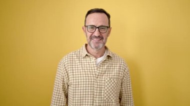 Middle age man smiling confident doing ok sign with thumbs up over isolated yellow background