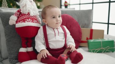 Sevimli İspanyol bebek, evdeki Noel ağacının yanında koltukta kendinden emin bir şekilde emekliyor.