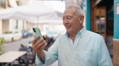 Senior grey-haired man smiling confident having video call at street