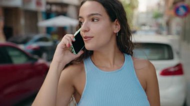 Genç, güzel, İspanyol bir kadın gülümsüyor ve caddede akıllı telefondan konuşuyor.