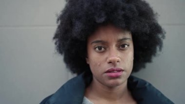 Afro-Amerikalı kadın, beyaz arka planda kendine gülerek duruyor.