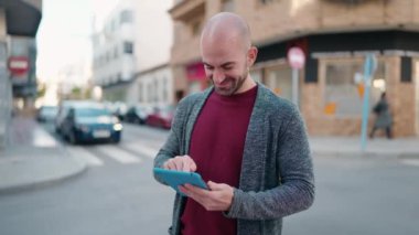 Young bald man smiling confident using touchpad at street