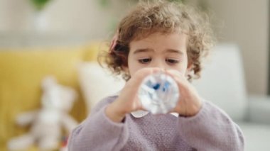 Adorable hispanic girl drinking water standing at home