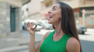 Genç, güzel, İspanyol bir kadın gülümsüyor ve caddede akıllı telefondan konuşuyor.
