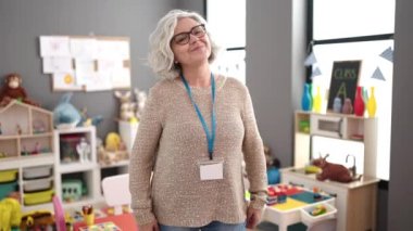 Middle age woman with grey hair preschool teacher smiling confident standing at kindergarten