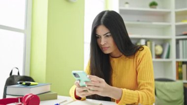 Kütüphanede akıllı telefon kullanan güzel İspanyol bir kız öğrenci.