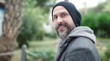 Genç kel adam parkta kendine güvenerek gülümsüyor.