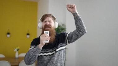 Young redhead man listening to music singing song at home