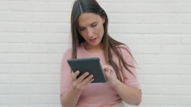 Genç ve güzel İspanyol kadın, izole edilmiş beyaz tuğla arka planda kazanan yüz ifadesi olan dokunmatik ped kullanıyor.