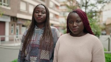 İki Afro-Amerikan kadını ciddi bir ifadeyle sokakta dikiliyorlar.