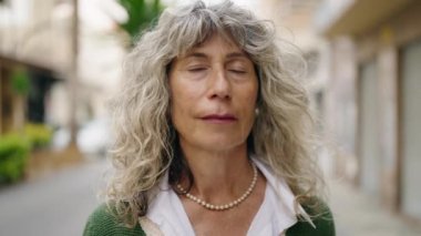 Orta yaşlı bir kadın sokakta kendine güvenerek gülümsüyor.