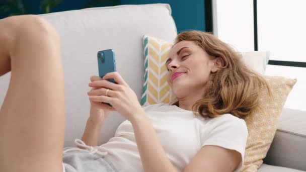 年轻美丽的惊慌失措的女人用智能手机躺在家里的沙发上 — 图库视频影像