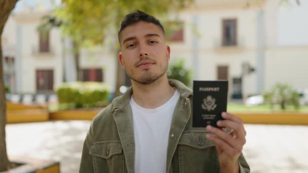 年轻的惊慌失措的男人带着自信的微笑指着公园里的美国护照 — 图库视频影像