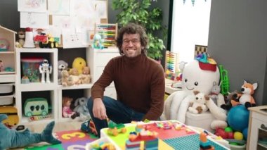 Young hispanic man preschool teacher smiling confident at kindergarten