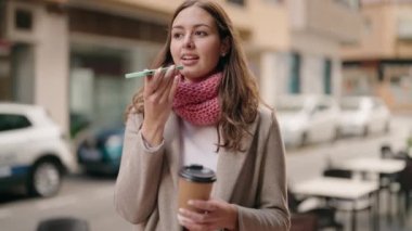 Young woman talking on the smartphone drinking coffee at street