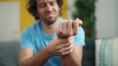 Young hispanic man sitting on sofa suffering for wrist pain at home