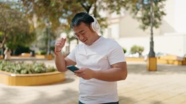 Young chinese man smiling confident listening to music at park