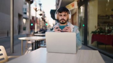 Young hispanic man playing video game sitting on table at coffee shop terrace