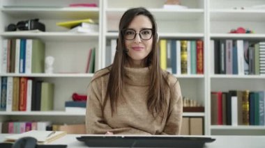 Güzel İspanyol bayan öğrenci kütüphane üniversitesinde video araması yaptığından emin bir şekilde gülümsüyor.
