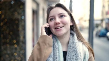 Genç sarışın kadın gülümsüyor. Kendine güveni tam. Akıllı telefondan konuşuyor.