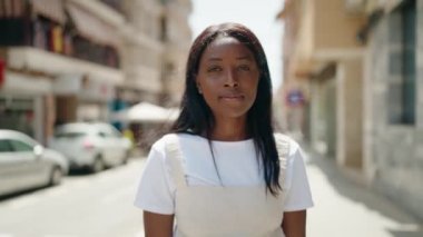 Genç Afrikalı Amerikalı kadın gülümsüyor. Kendine güveni tam. Sokakta kollarını kavuşturmuş duruyor.