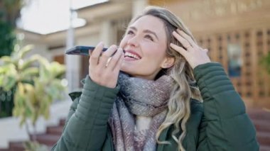 Young blonde woman sending voice message with smartphone at street
