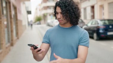 Genç Latin adam gülümsüyor. Kendine güveni tam. Sokakta akıllı telefondan selfie çekiyor.