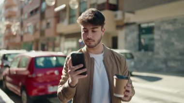 Genç İspanyol adam akıllı telefon kullanıyor, sokakta kahve içiyor.