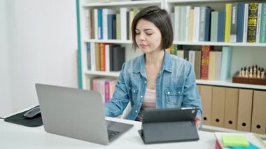 Genç beyaz kız öğrenci üniversite sınıfında ders çalışırken dizüstü bilgisayar ve dokunmatik ped kullanıyor.