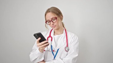 Sarışın kadın doktor, izole edilmiş beyaz arka plan üzerinden akıllı telefon kullanarak gülümsüyor.